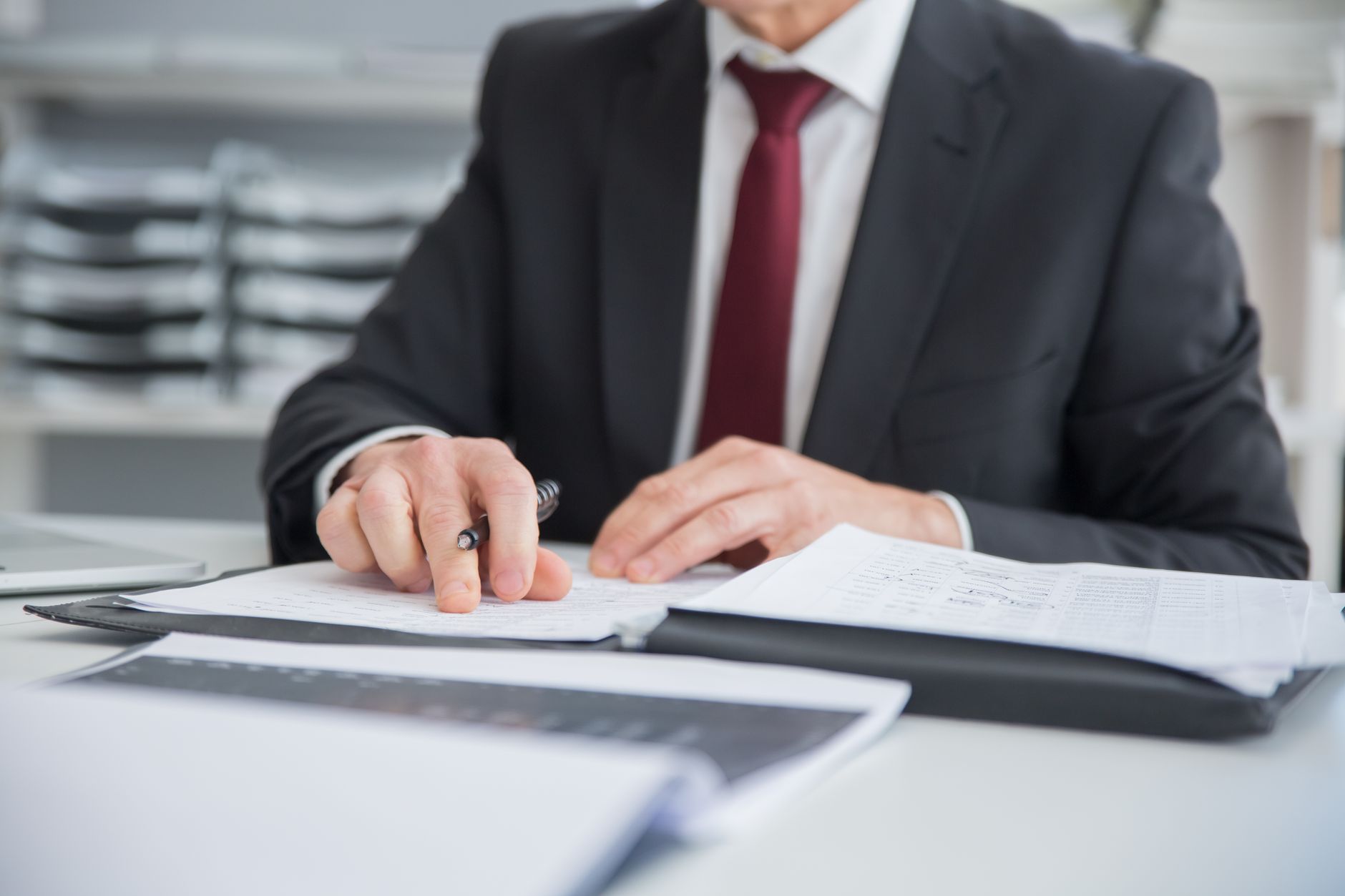 A compliance analyst reviewing documents at an office desk, hands and paperwork in focus